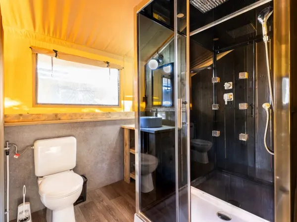 La salle de bain du Roan Lodgetent Premium XL est équipée d'une cabine de douche de luxe, de toilettes et d'un lavabo.