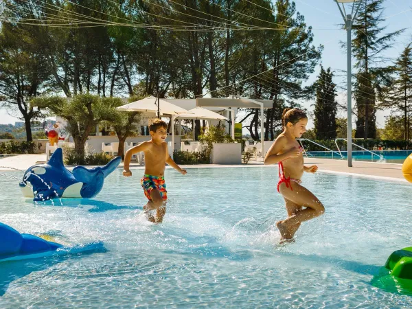 Enfants courant dans la piscine peu profonde du camping Roan Valkanela.