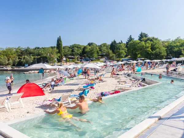 Piscine à débordement sur la plage de sable du camping Roan Lanterna.