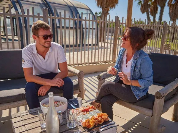 2 personnes prennent un verre sur la terrasse du Roan camping Les Dunes.