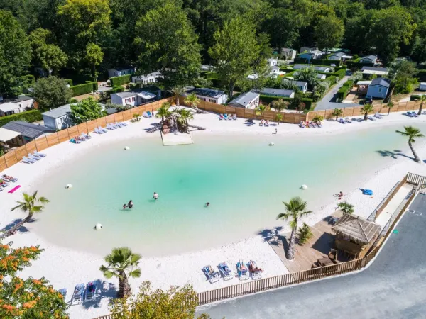 Vue d'ensemble de la piscine lagon avec plage de sable au Roan camping La Clairière