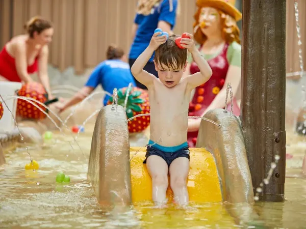 Petit garçon s'amusant dans l'eau depuis le toboggan de la pataugeoire du camping Roan Terspegelt.