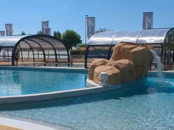 Piscine couverte et piscine extérieure avec cascade au camping Roan Le Domaine du Clarys.
