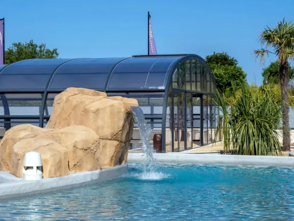 Piscine couverte et piscine extérieure avec cascade au camping Roan Le Domaine du Clarys.