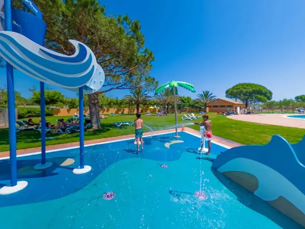 Parc à jets d'eau et aire de bronzage avec des chaises longues à l'ombre au camping Roan Platja Brava.