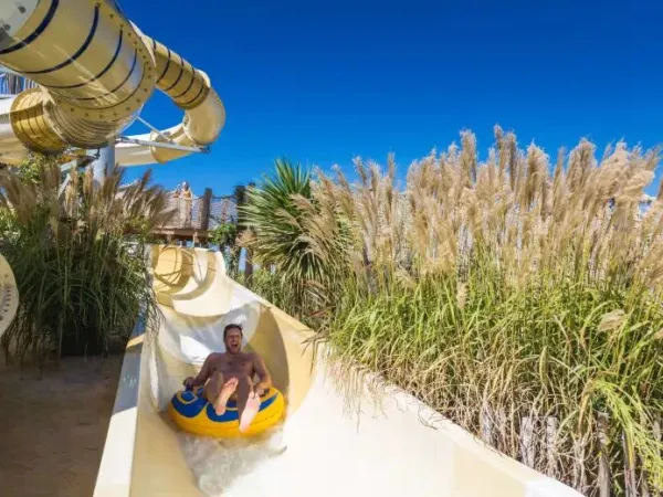 Le père s'amuse à glisser sur le toboggan à pneus du camping Roan Le Serignan Plage.