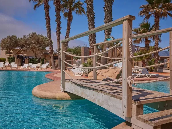 Pont et chaises longues au bord de la piscine du camping Roan Le Petit Mousse.