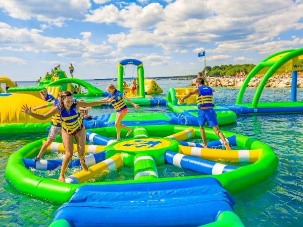 Des enfants jouent sur des coussins d'air dans le lac au camping Roan Le Lac des Vieilles Forges.