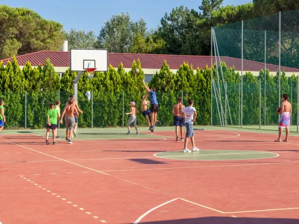 Les enfants jouent au basket sur le terrain multisports du camping Roan Marina Julia Camping Village.