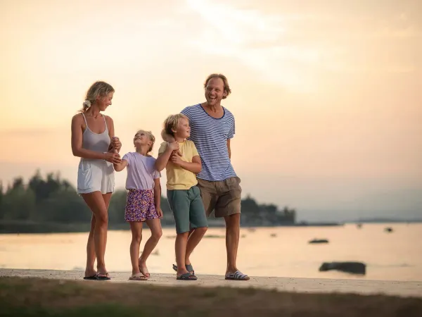 Famille souriante marchant sur la plage au coucher du soleil.